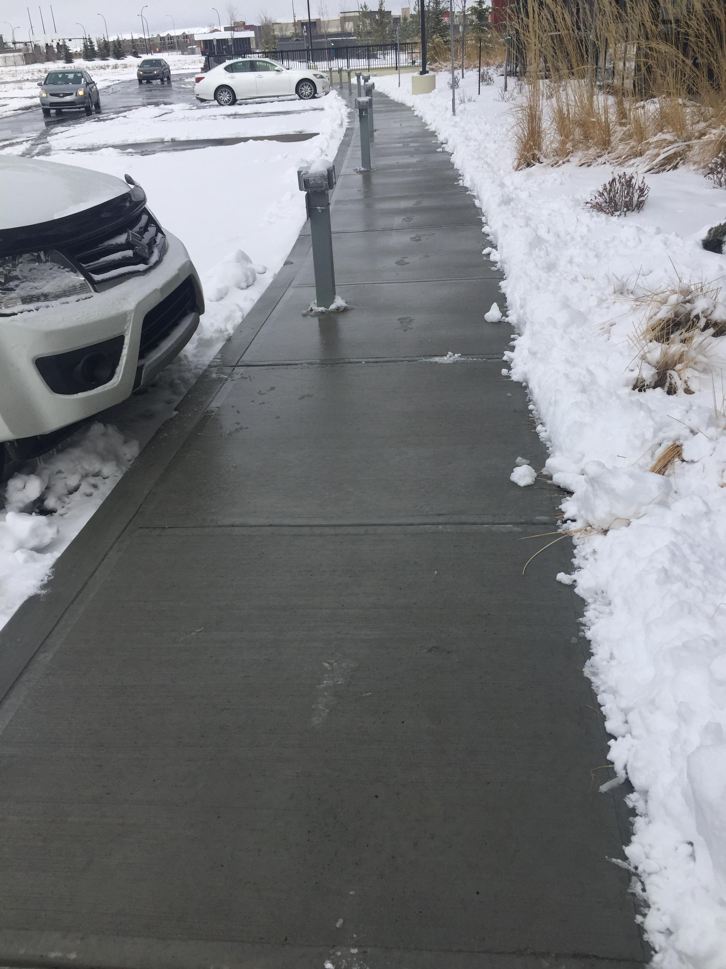 Commercial walkway cleared alongside parking lot with snow banks visible